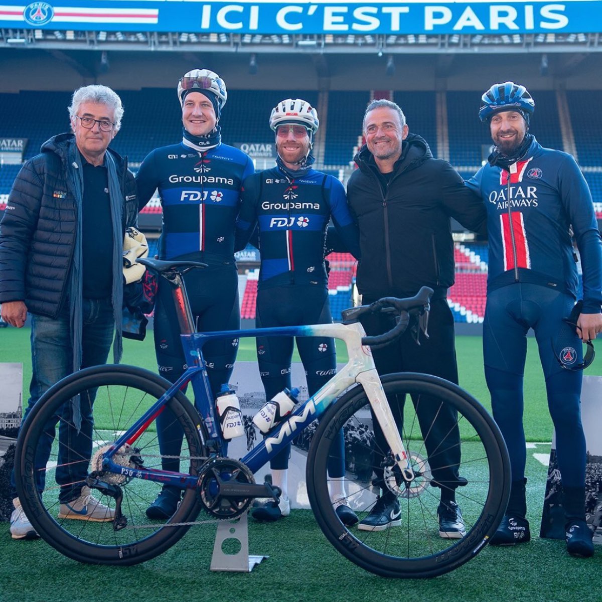 Groupe réuni sur la pelouse du Parc des Princes autour d'un vélo de route, trois cyclistes casqués