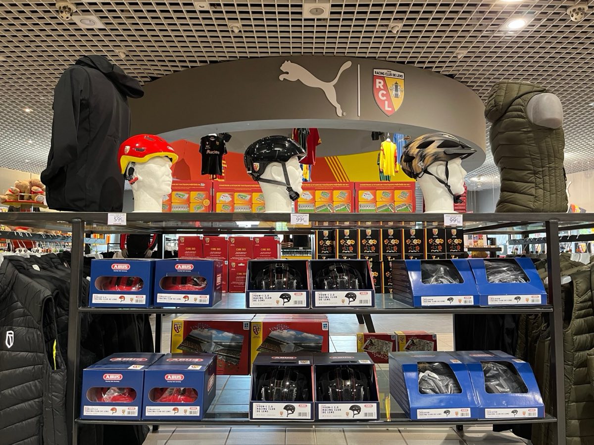 Étagère de boutique où trois casques du RC Lens sont posés sur des têtes de présentation, leurs boîtes rangées en dessous
